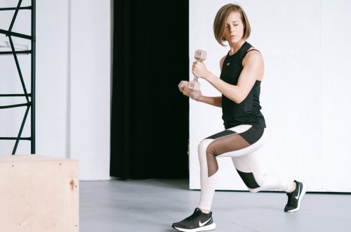 A young woman performing lunges with dumbbells in a modern indoor gym setting.